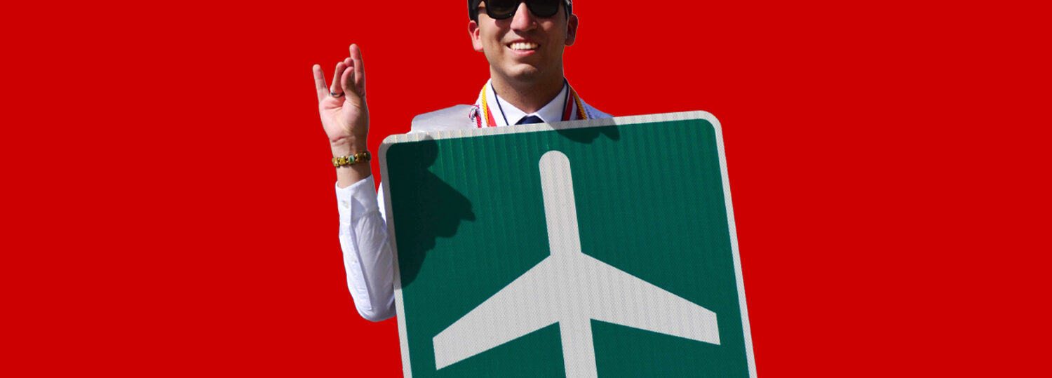 Alberto Quiroga wearing his red graduation cap and holding a green and white airplane directional road sign.