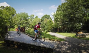 Image shows two cyclists on a path near Lake Raleigh.