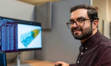 Dariush Heiranian sitting at a desk in front of a monitor running a program.