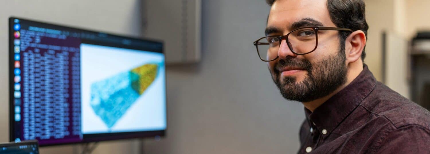 Dariush Heiranian sitting at a desk in front of a monitor running a program.