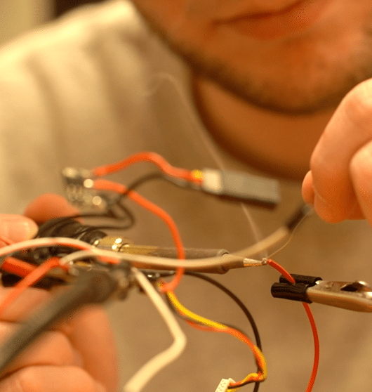 Image is a close-up of a man handling red and yellow wires.
