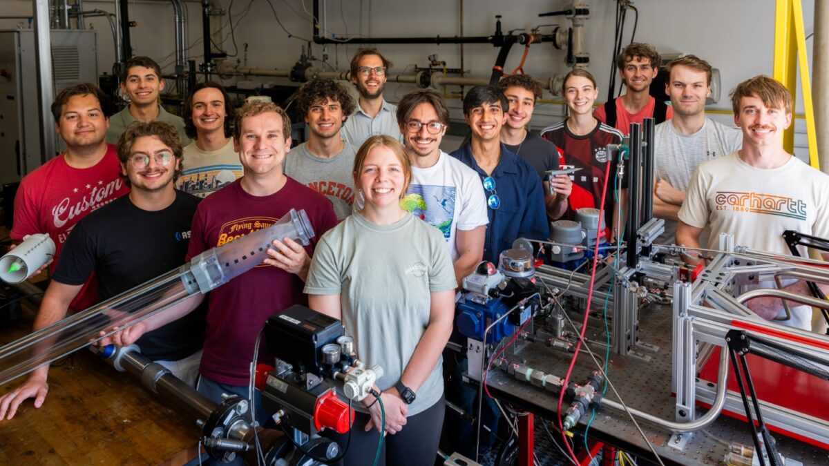 A group of people in a warehouse type lab, standing around equipment.