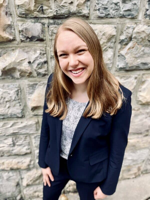 Mackenzie Perry in a black blazer with a stone wall behind her.